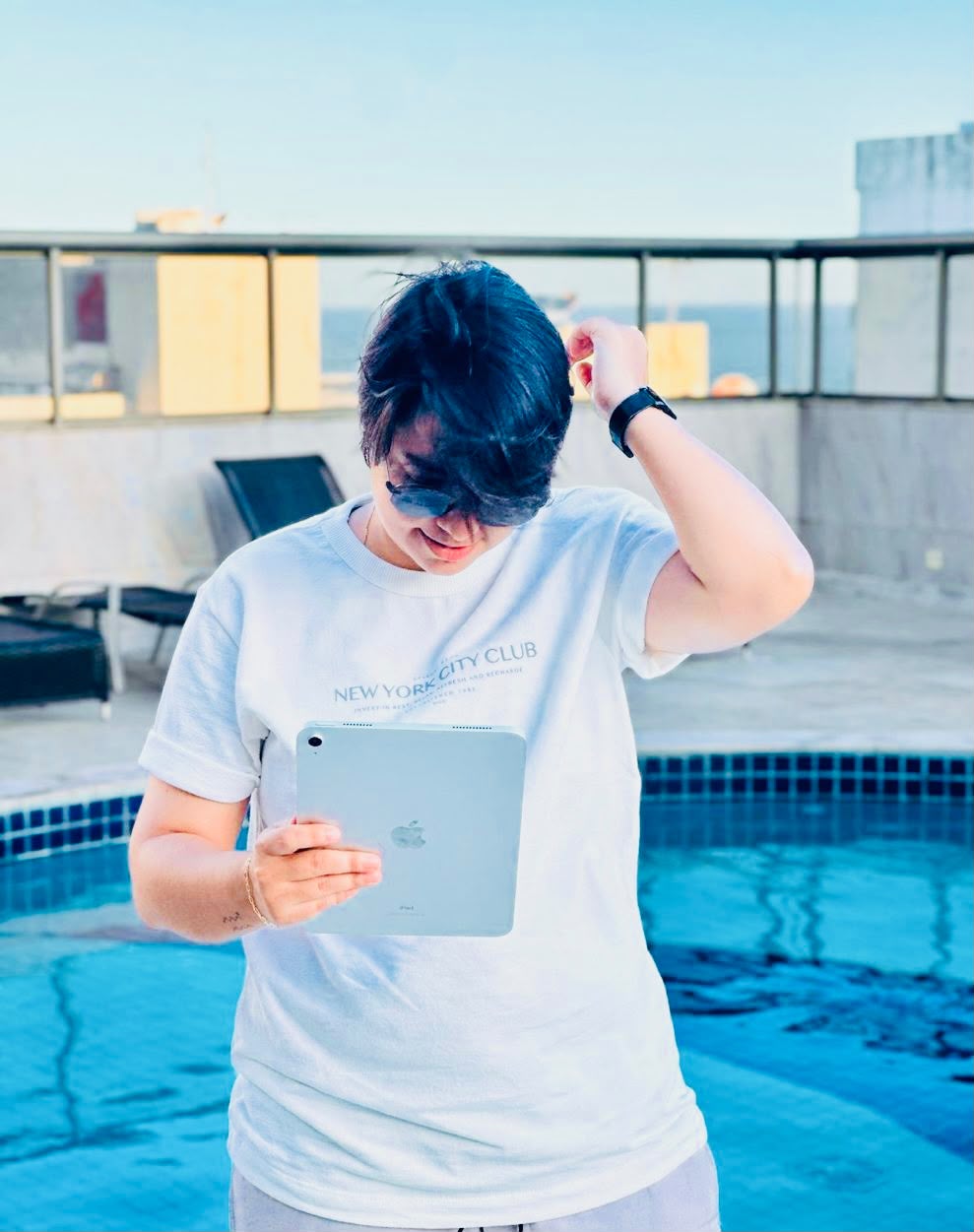 Gessica com tablet à beira da piscina, ajeitando o cabelo.