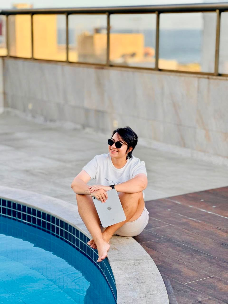 Gessica sentada à beira da piscina com um tablet.