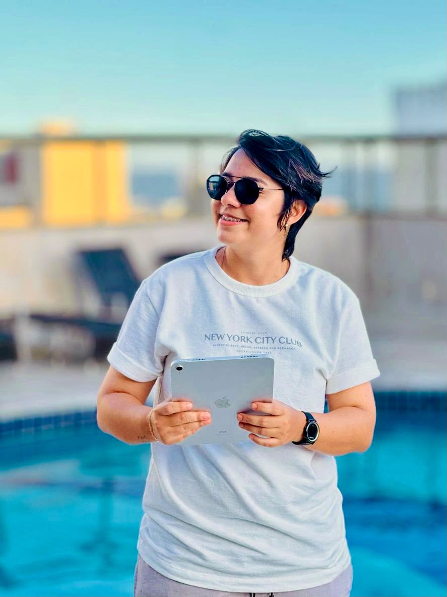 Gessica de óculos escuros segurando um tablet à beira da piscina.