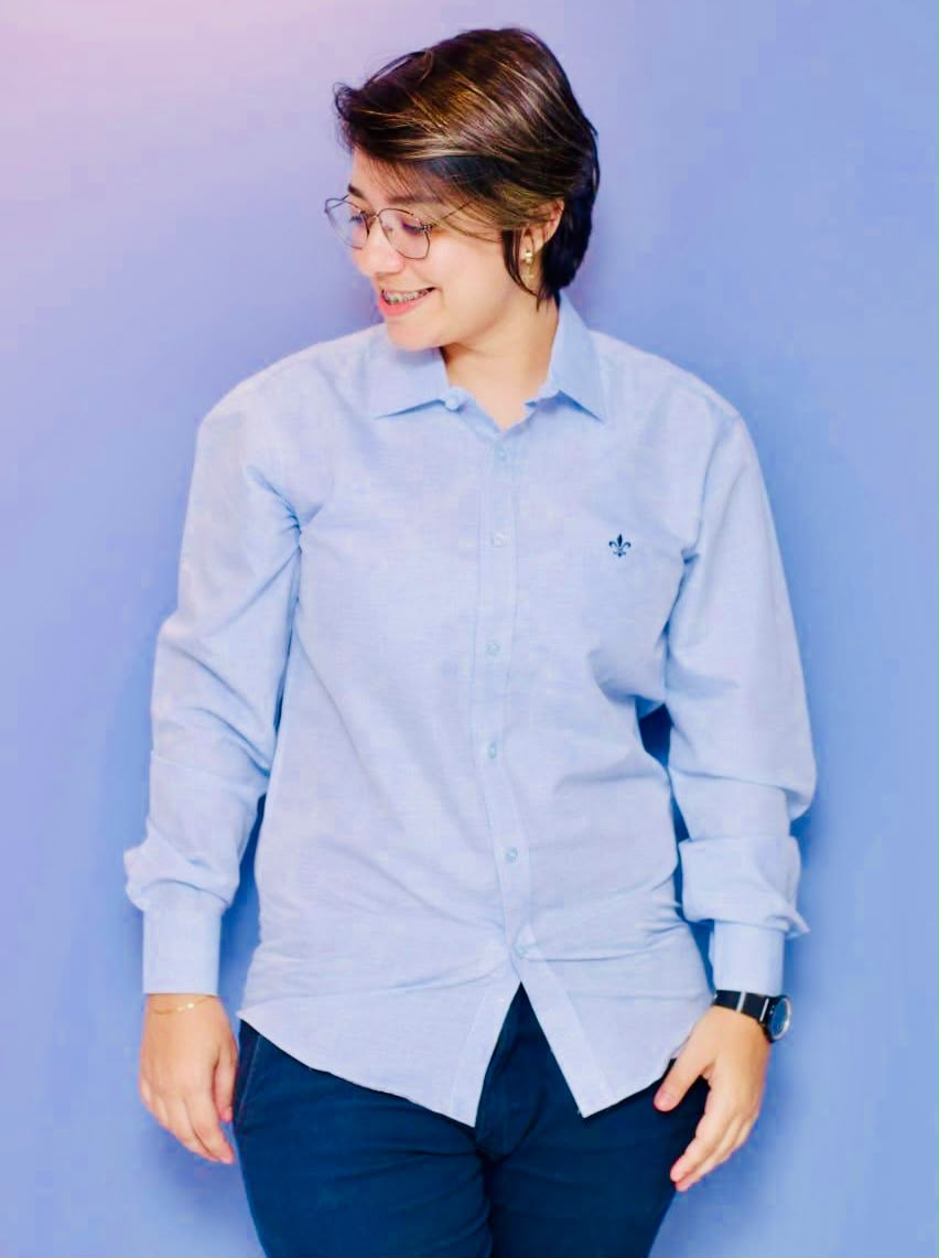 Gessica em pé, de camisa azul, sorrindo e olhando para o lado.